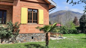A brick house with yellow shutters, a stone foundation, and a view of mountains in the background. - La Villa Luchonnaise, 5mn du Centre Ville, Télécabine et Thermes (Bagnères-de-Luchon)