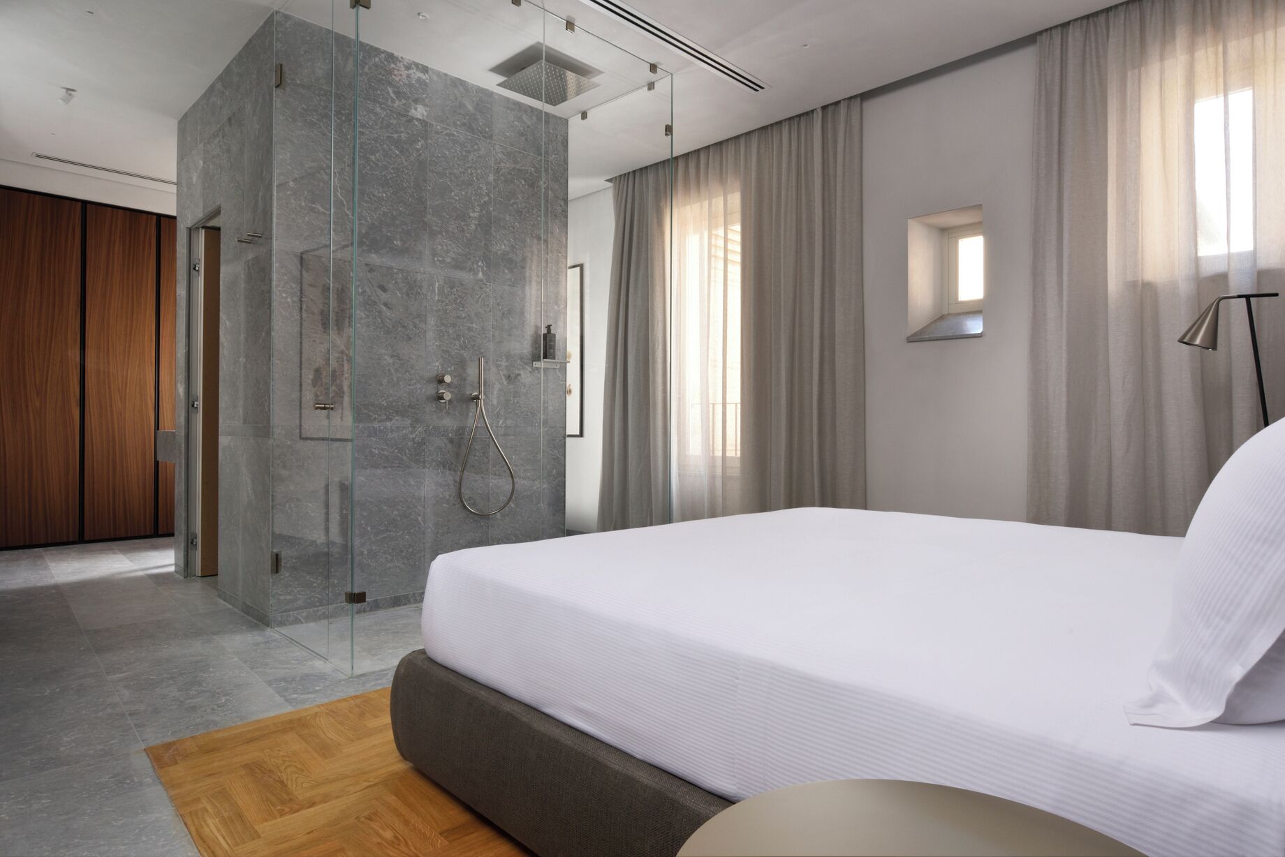 A modern hotel room with a large bed, a glass-enclosed shower, and a view of the outside.