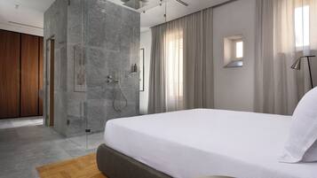 A modern hotel room with a large bed, a glass-enclosed shower, and a view of the outside.