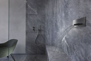 Un baño moderno con ducha, paredes de mármol y mampara de vidrio.