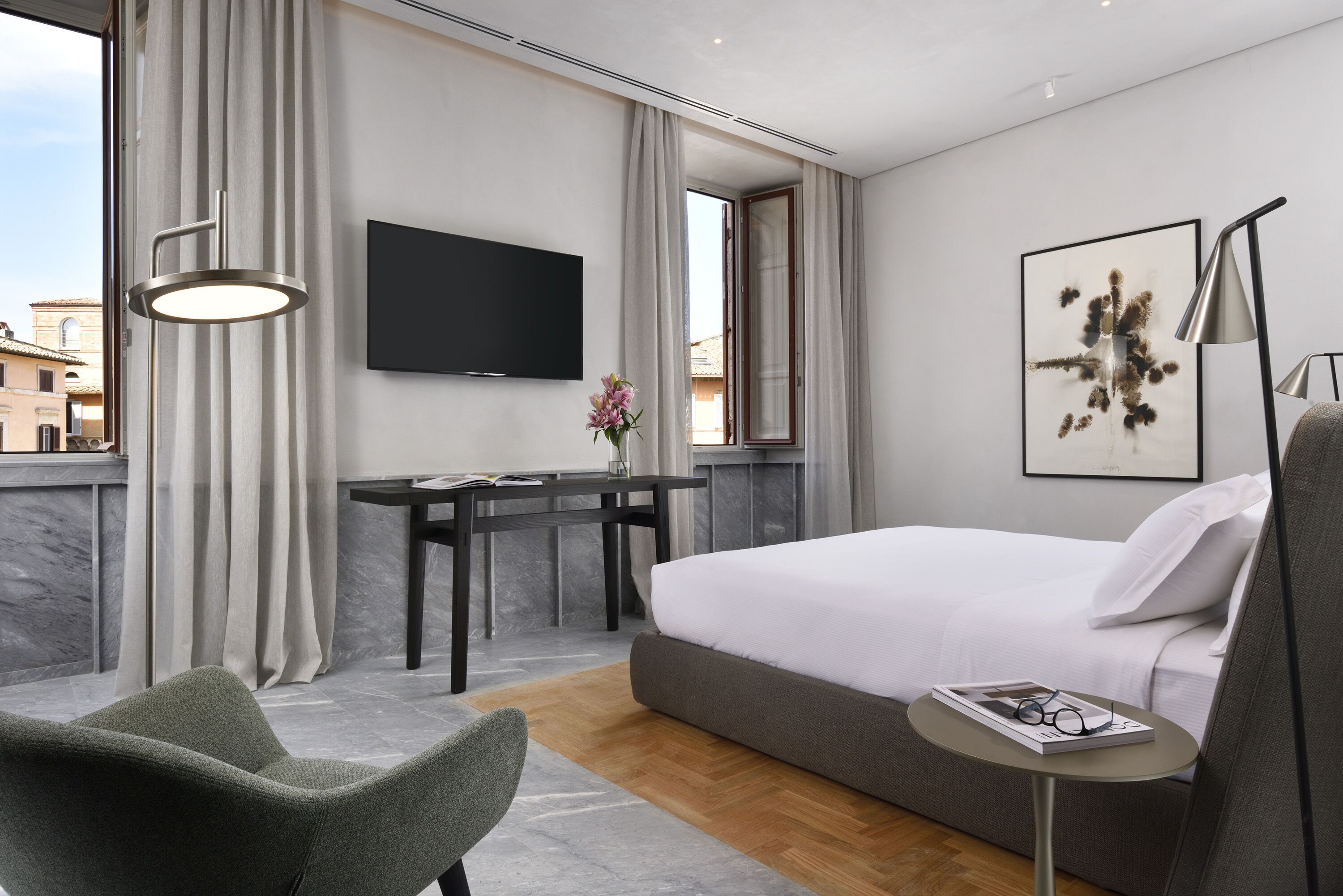 A modern hotel room with a bed, a desk, a chair, a TV, and a window with curtains.