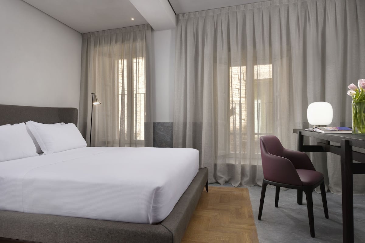 A hotel room with a large bed, a desk with a chair, and a lamp.