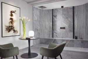 Un vestíbulo moderno con un mostrador de recepción de mármol, dos sillones verdes, un jarrón con flores blancas y un cuadro abstracto enmarcado.