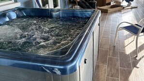 A hot tub in a covered outdoor area with tiled flooring and a person sitting nearby.
