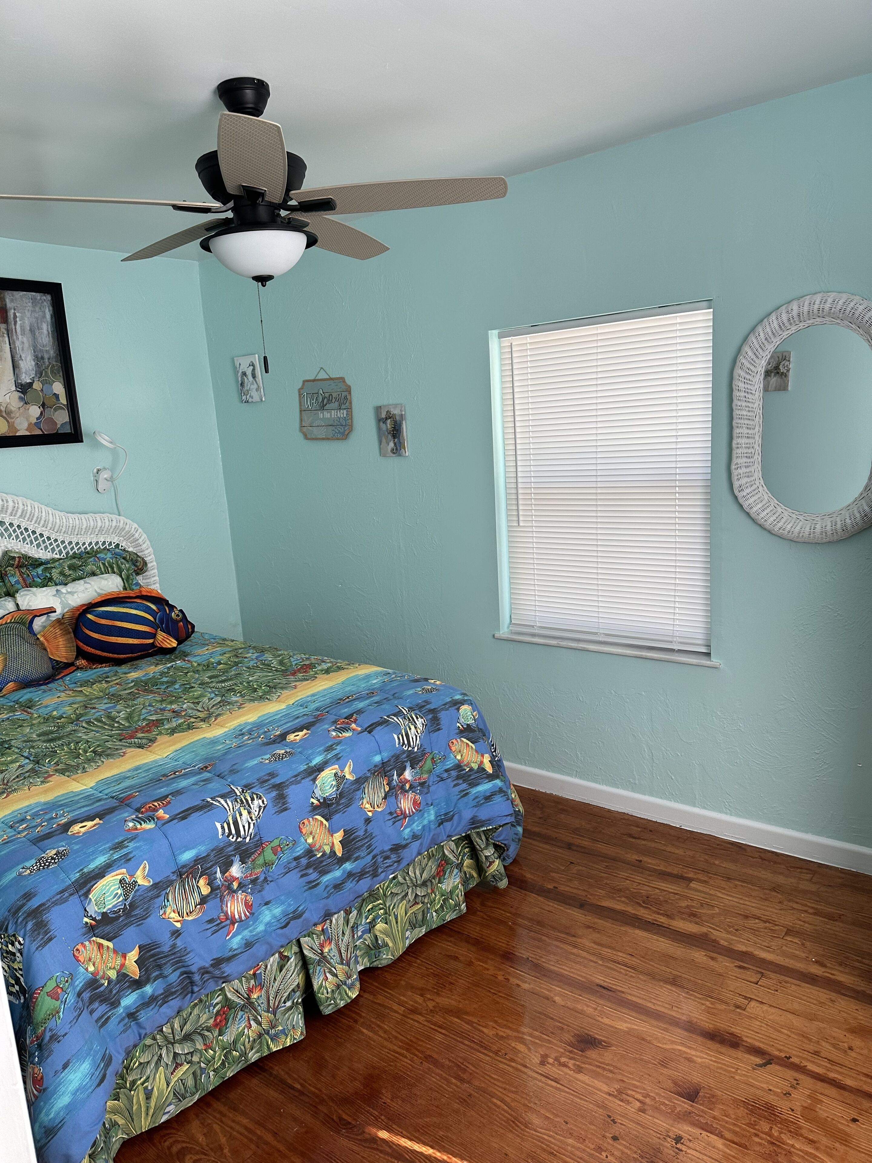 Un dormitorio con cama, ventilador de techo, ventana con persianas y adornos en la pared.