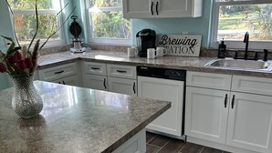 A kitchen with white cabinets, granite countertops, and a coffee maker.
