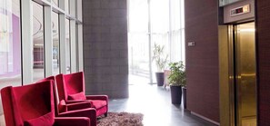 A hallway with red chairs, a potted plant, and an elevator.