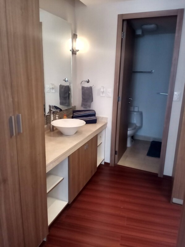 A bathroom with a wooden vanity, a large mirror, a sink, and a toilet visible through an open door.