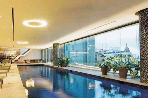 A modern indoor pool with a city view, large windows, and potted plants.
