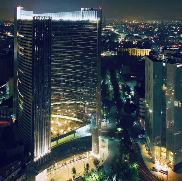 A high-rise building with a curved glass facade, surrounded by a well-lit urban area at night.