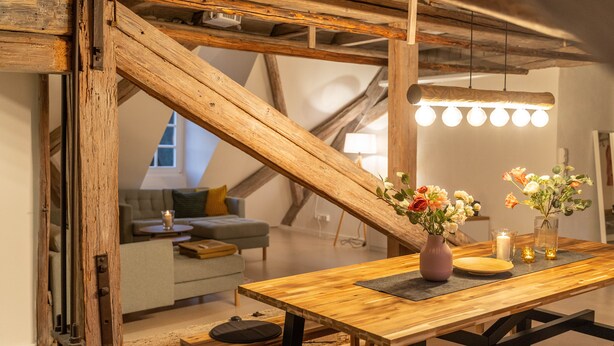 Une table à manger en bois, ornée d’un vase de fleurs, de bougies et d’un luminaire suspendu au design moderne.