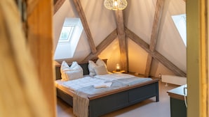 Une chambre avec un plafond en pente, un lit avec des oreillers, une table de chevet et un luminaire suspendu.