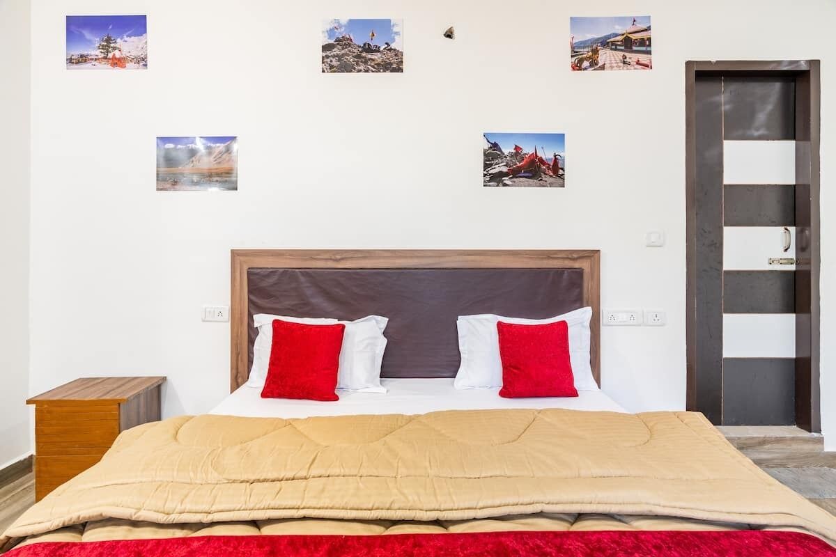 A hotel room with a large bed, two red and two white pillows, a wooden nightstand, and a door with a black and white panel.