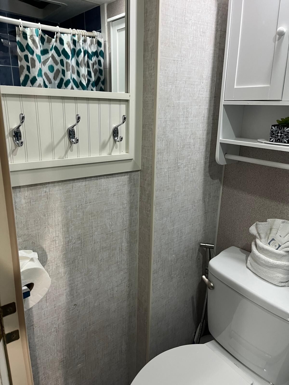 A bathroom with a toilet, a shower curtain, a towel rack, and a small shelf with a decorative item.
