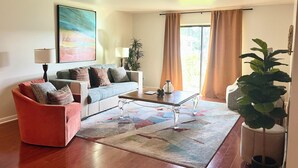 A living room with a sofa, armchair, coffee table, and potted plants.