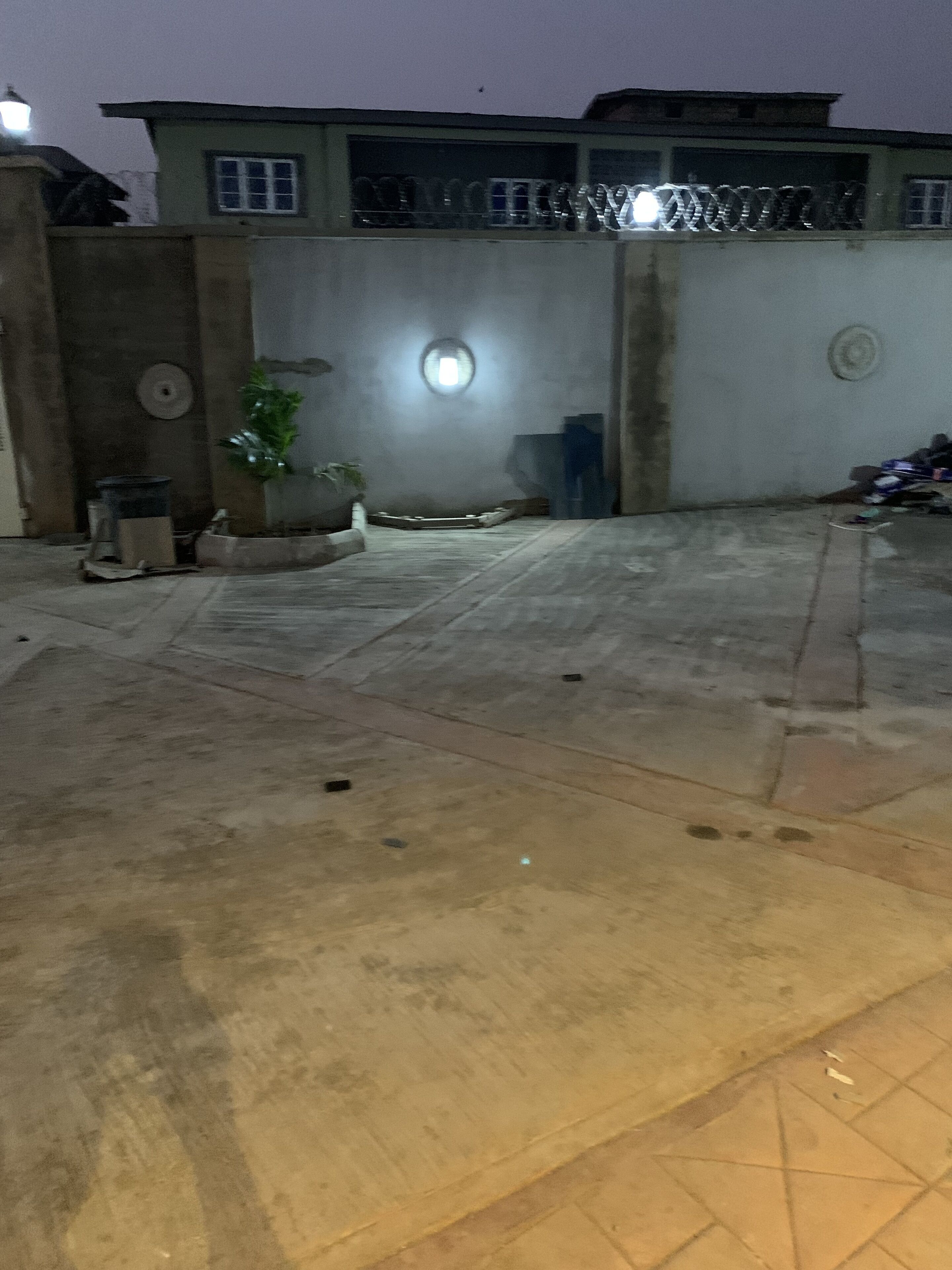 A courtyard with a tiled floor, a potted plant, and a wall with a circular window.