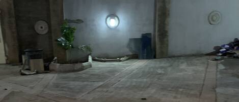A courtyard with a tiled floor, a potted plant, and a wall with a circular window.