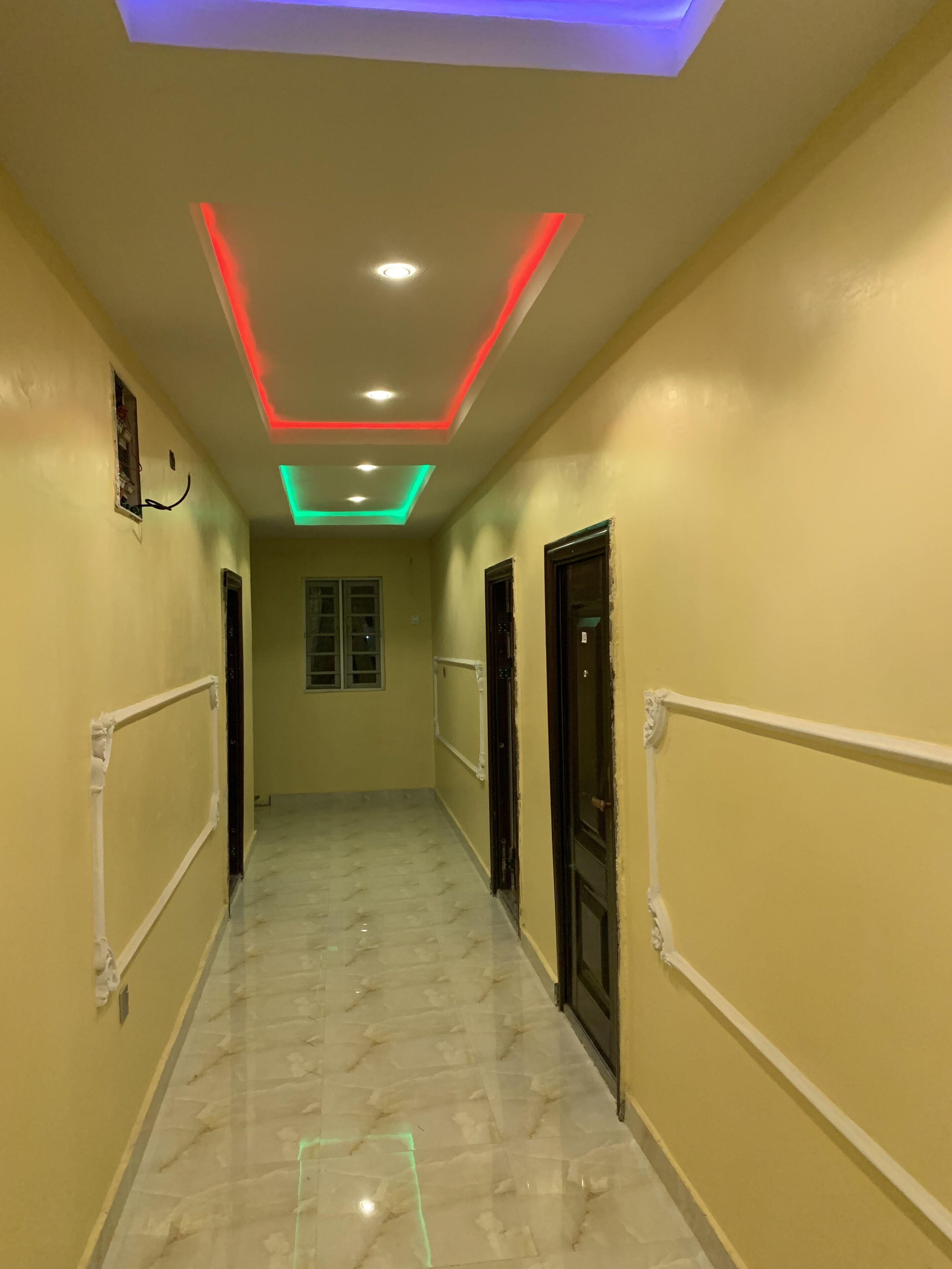 A hallway with a marble floor, yellow walls, and doors on both sides.