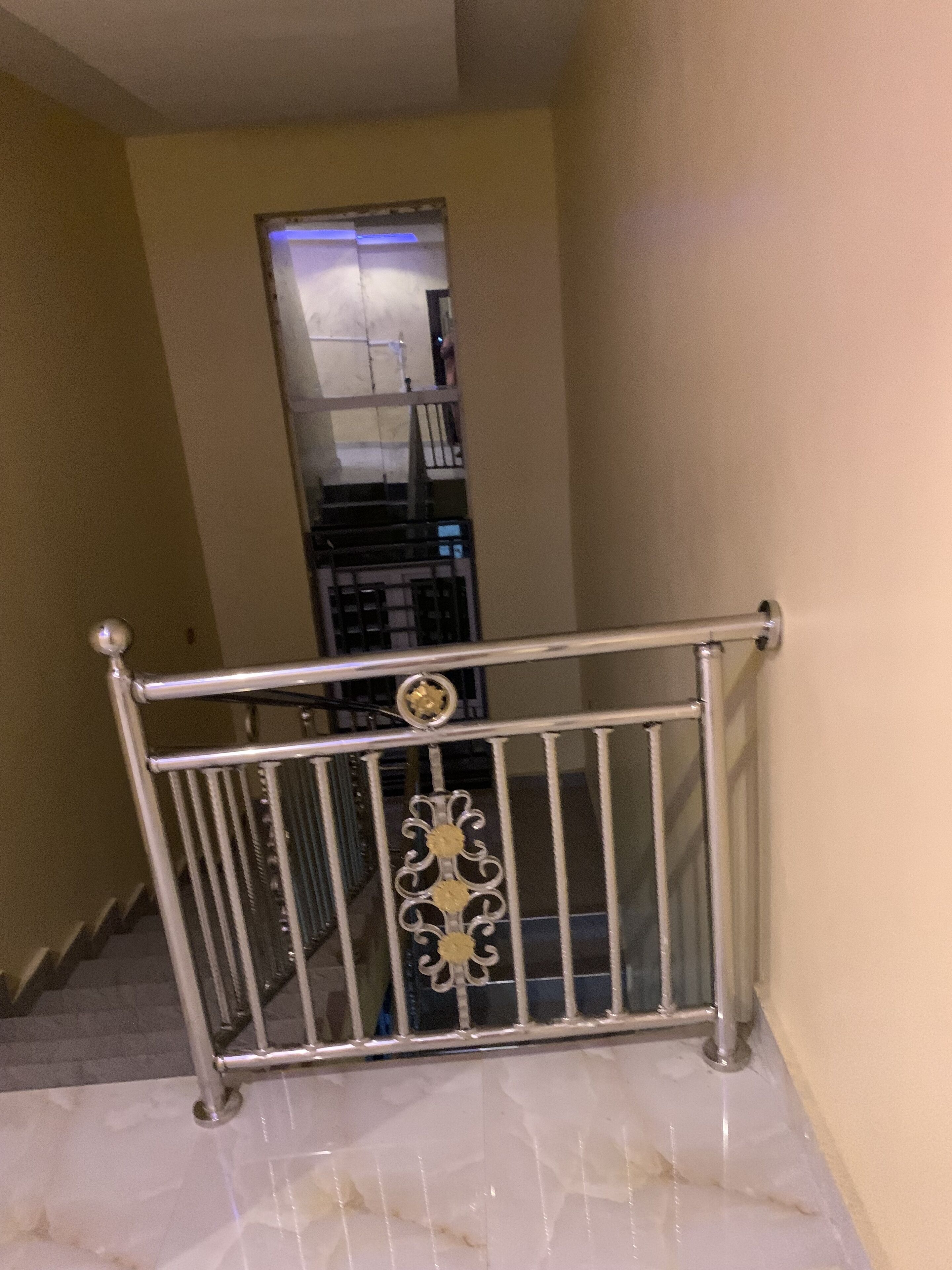 A staircase with a metal railing, a tiled floor, and a beige wall.