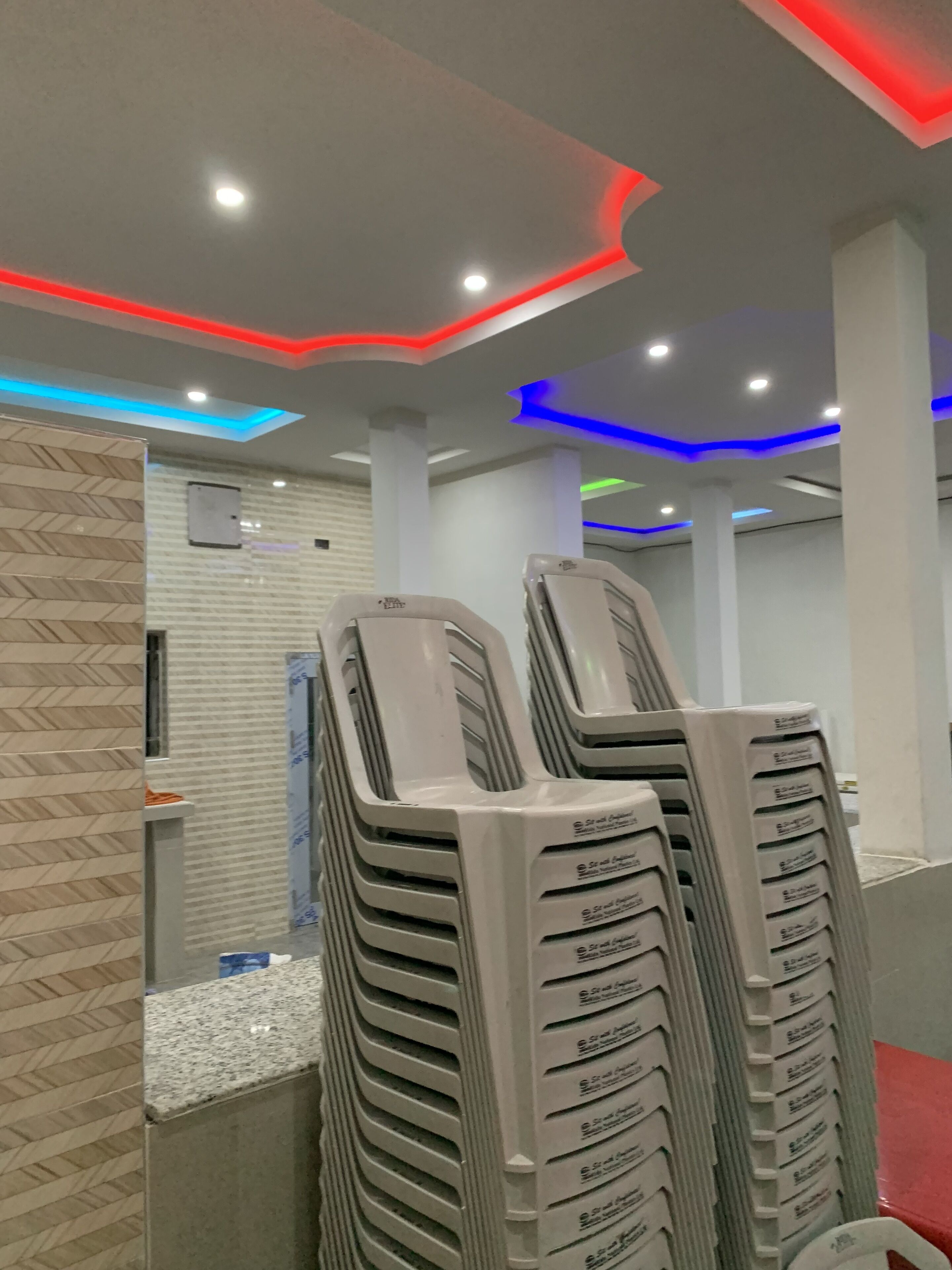 A stack of plastic chairs in a room with a modern ceiling design featuring recessed lighting and colored LED accents.