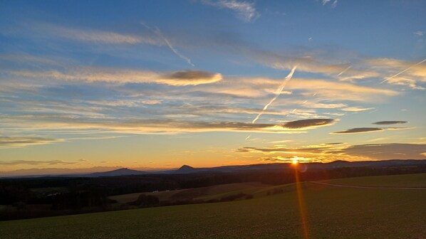 Un atardecer sobre un paisaje montañoso con cielo despejado y estelas visibles.