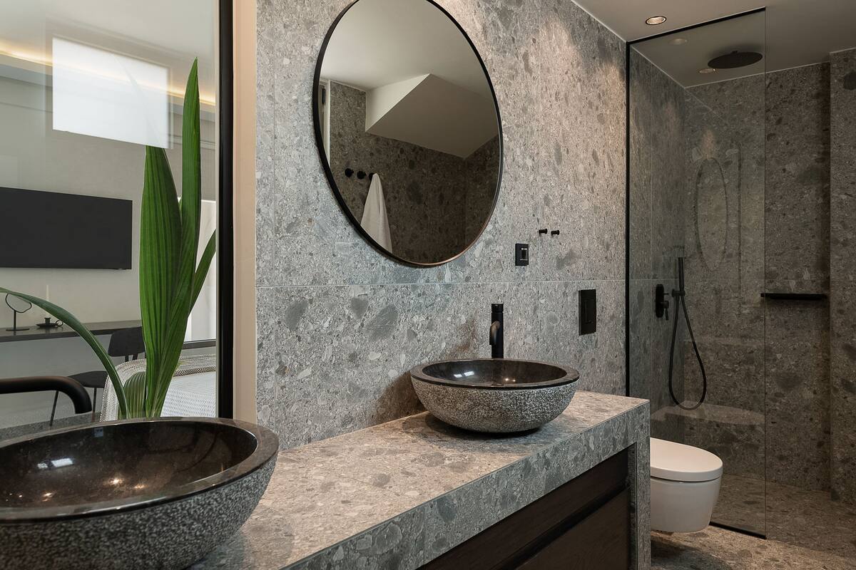 Un baño con un lavamanos de piedra, un espejo redondo y una zona de ducha.