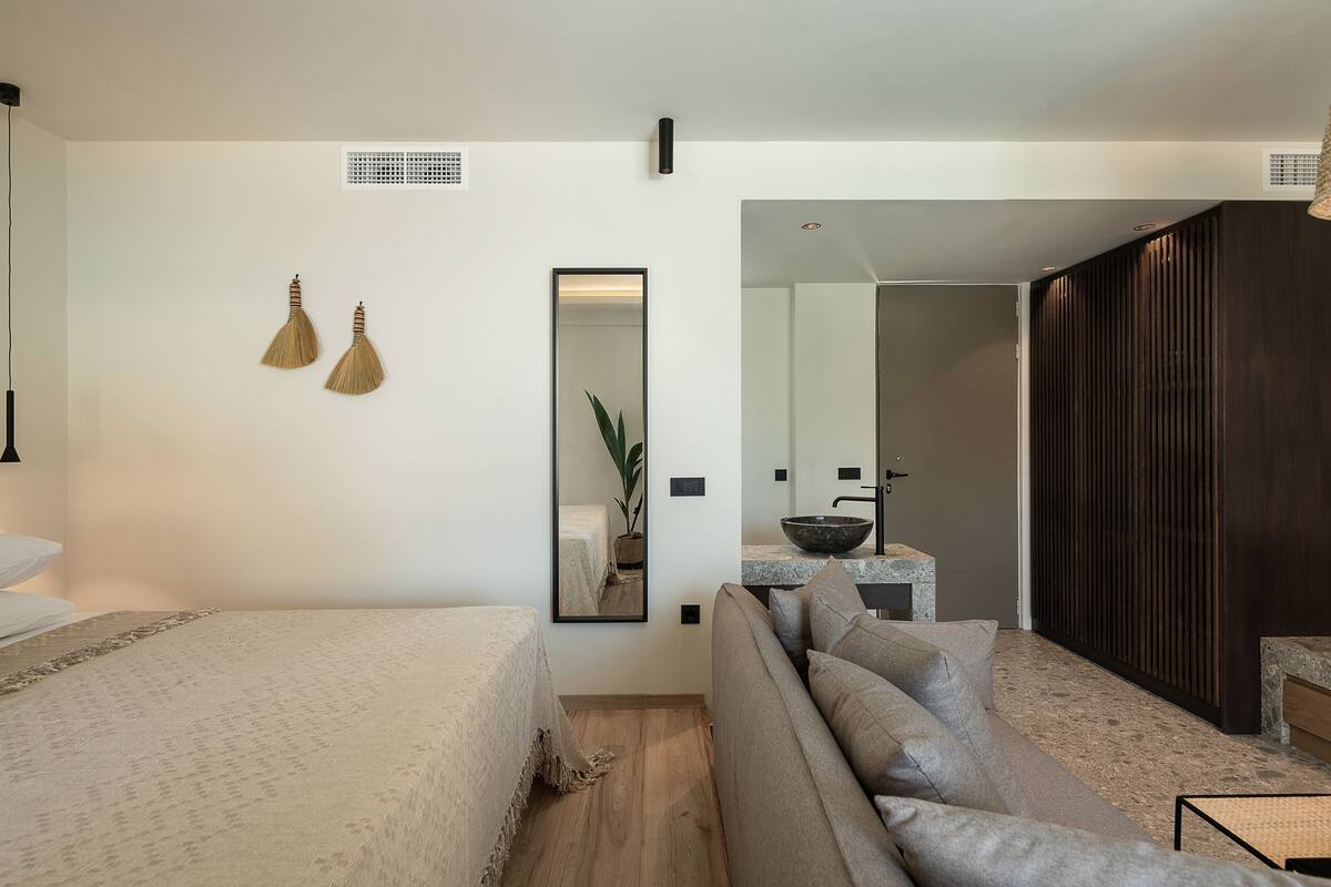 Una habitación de hotel moderna con una cama, un sofá, un espejo y una pequeña cocina.