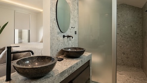 A modern bathroom with a large oval mirror, two vessel sinks, a black faucet, and a glass shower enclosure. - Casa Nostos (Chania)