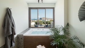A modern bathroom with a large bathtub, a view of the sea, and a potted plant. - Casa Nostos (Chania)