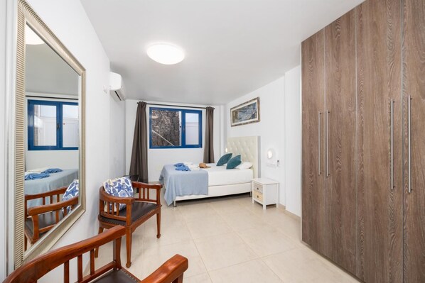 A bedroom with a bed, a wooden wardrobe, a bedside table, a chair, a mirror, and a window with curtains. - Villa Beyond - Three Bedroom Villa, Sleeps 6 (Playa Blanca)
