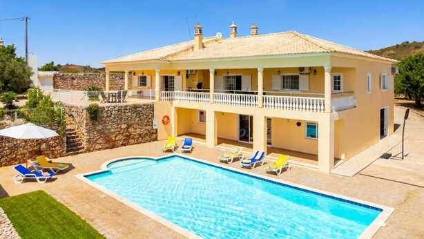 Un edificio a due piani con piscina, area salotto all'aperto e un muro in pietra.