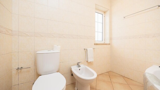 Et lille badeværelse med toilet, bidet og et vindue.