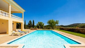 Una piscina con lettini, un portico coperto e vista su alberi e colline.
