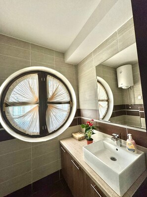Une salle de bain moderne avec une fenêtre ronde, un lavabo, un miroir et un porte-serviettes.