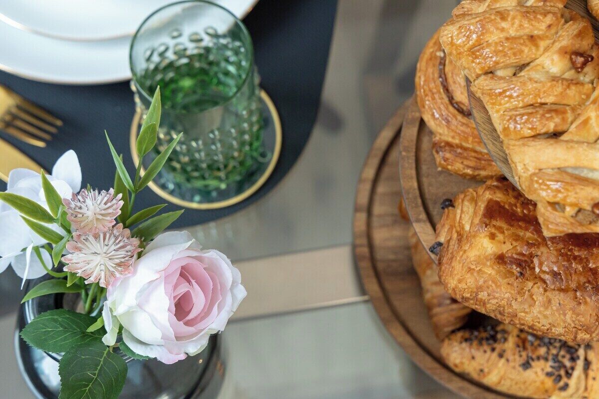 Ein gedeckter Tisch mit Blumenarrangements, einem Glas Wasser und einer Holzbrett mit Gebäck.