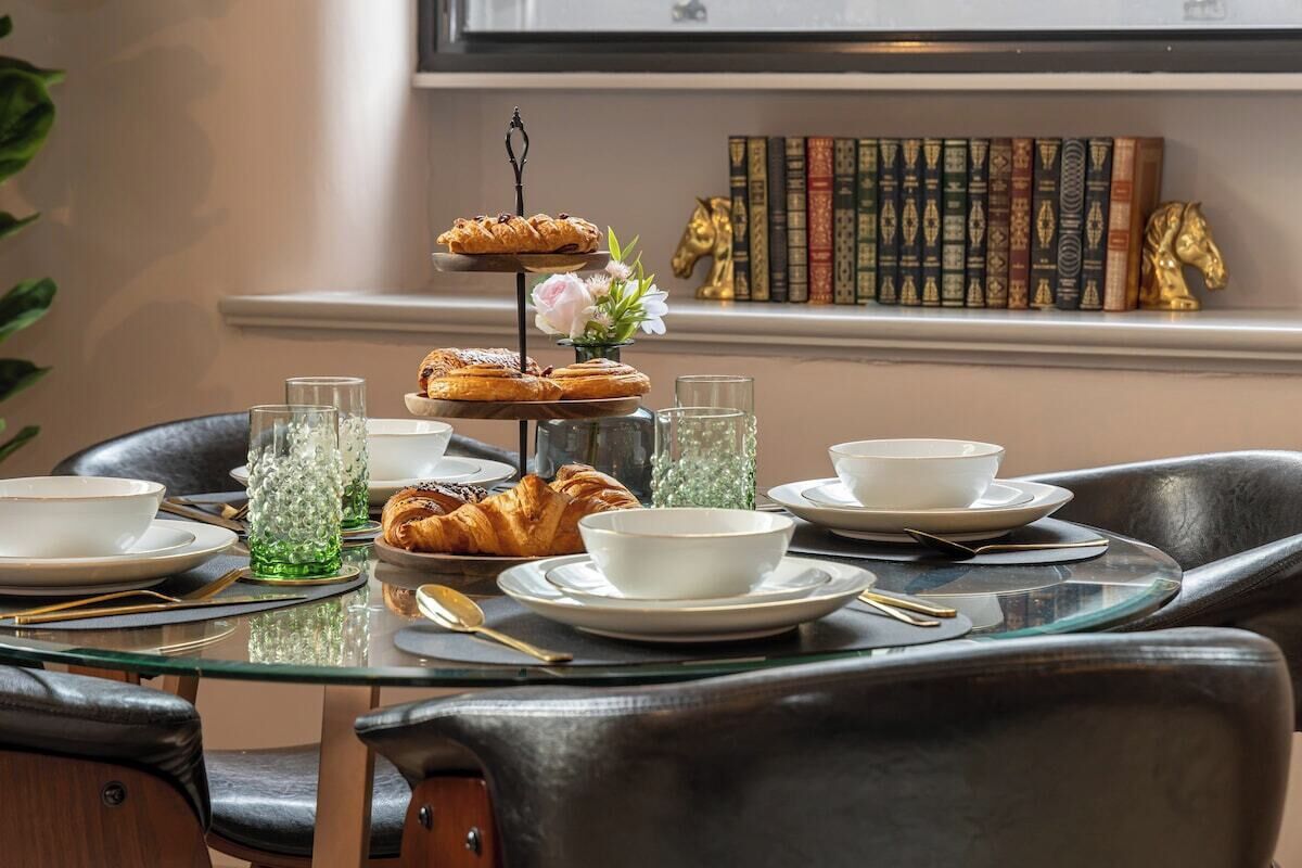 A three-tiered dessert stand with pastries and a flower, surrounded by white bowls and glasses on a glass table.