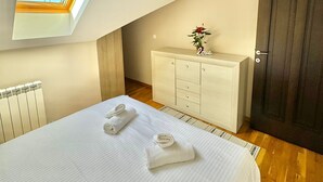 Un dormitorio con tragaluz, cama con toallas, cómoda de madera y una puerta oscura.