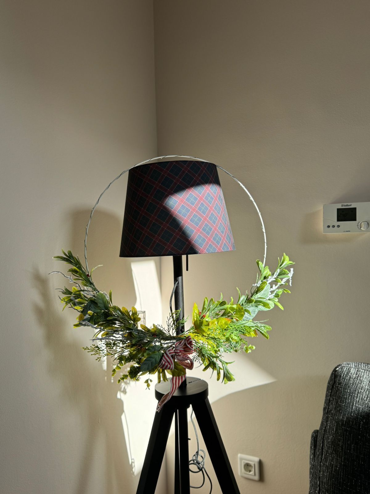 Eine Stehlampe mit Karoschirm und dekorativem Kranz auf einem Dreibeinstativ.