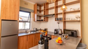 Una cucina moderna con mobili in legno, un frigorifero in acciaio inossidabile, un lavello e un piano di lavoro con bottiglie di vino e una ciotola di frutta.