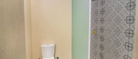 Un baño con inodoro, ducha y pared con diseño.