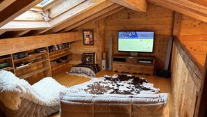 Un acogedor dormitorio en el ático con paredes de madera, un televisor, una estantería y un sofá cómodo.