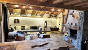 Un interior rústico con una mesa de comedor de madera, sillas de cuero, una chimenea de piedra y una zona de estar acogedora con un sofá y cojines.