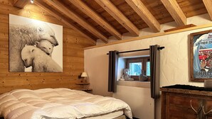 Un dormitorio con una cama grande, vigas de madera en el techo, una ventana con cortinas, un osito de peluche y un cartel en la pared.