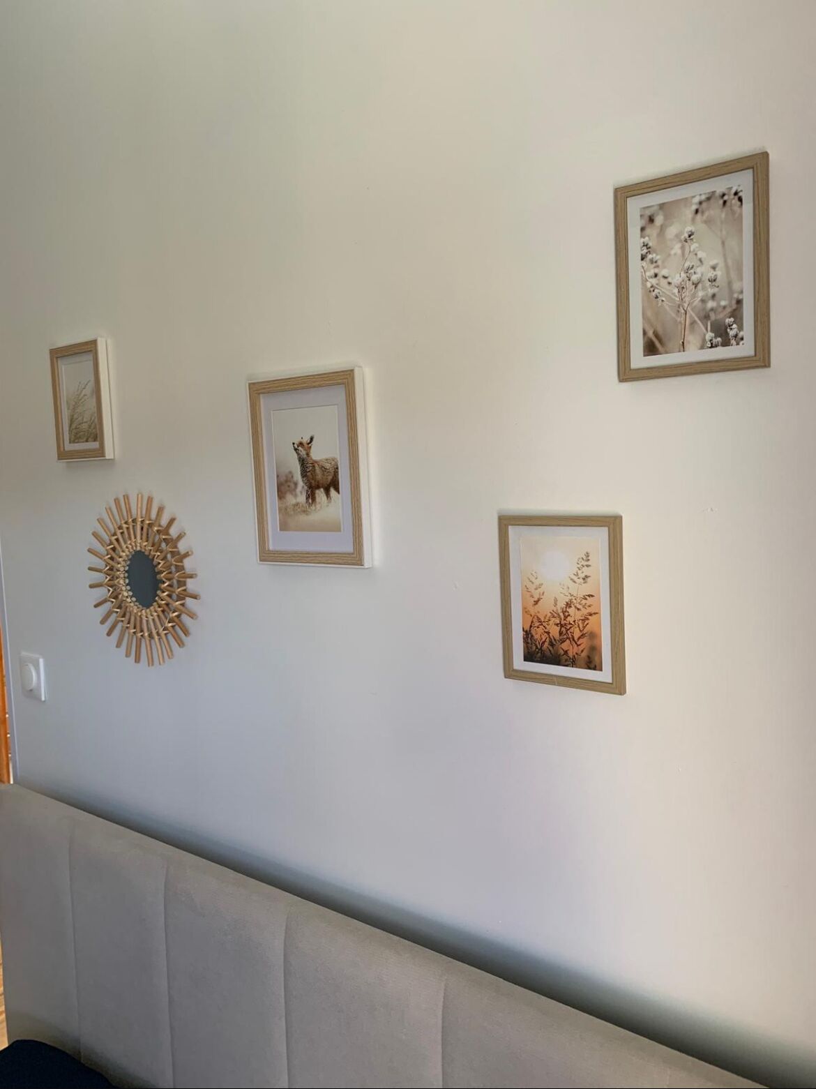 Een muur met vier ingelijste foto's, een spiegel in zonmodel en een bank.