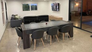 A modern living room with a dining area, a sofa set, a flat-screen TV, and a sliding glass door leading to a balcony. - Quelque Part au Calme (Beaumé)