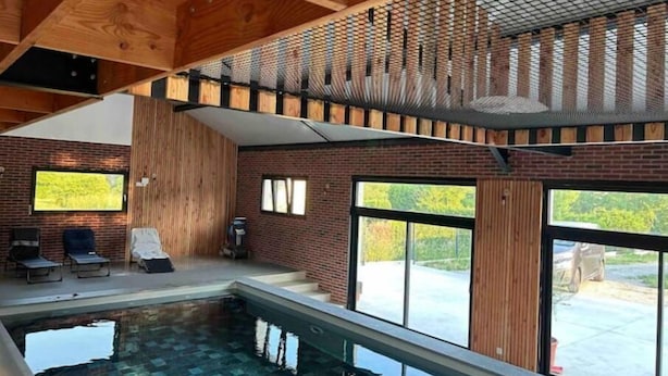 A modern indoor pool area with a wooden ceiling, brick walls, and large windows. - Quelque Part au Calme (Beaumé)