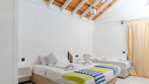 Ein modernes Schlafzimmer mit zwei Betten, Holzbalken an der Decke und einem großen Fenster mit Vorhängen.