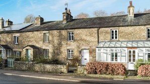A stone building with multiple chimneys, a small garden with shrubs, and a road in front. - 2 bedroom accommodation in Burrow, near Kirkby Londsdale (Burrow, near Kirkby Londsdale)