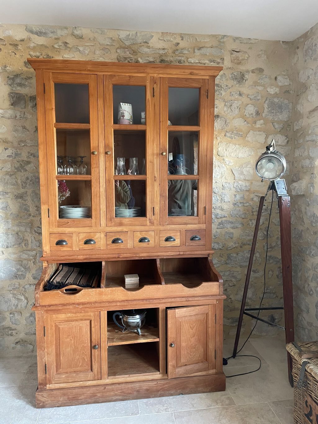 A wooden cabinet with multiple drawers and shelves, placed against a stone wall.