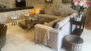 Un salon avec un mur en pierre, un canapé, une table basse en verre, des paniers en osier et un vase rempli de fleurs.